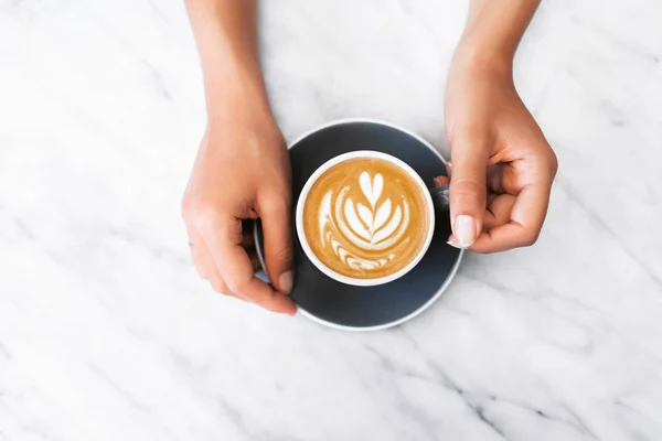 Žena ruce drží šedý šálek čerstvého cappuccino s klasickou la — Stock fotografie
