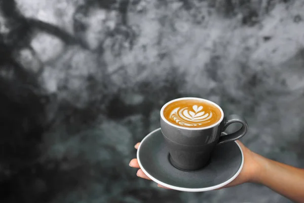 Žena drží v ruce šedý šálek čerstvého cappuccino na pozadí — Stock fotografie