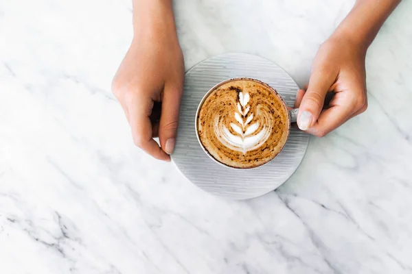 Xícara de cappuccino café fresco em mãos de mulher em mármore branco ta — Fotografia de Stock