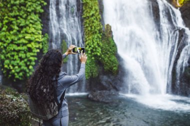 Bali 'deki Banyumala şelalesinin fotoğrafını çeken kadın. Uzun kıvırcık 