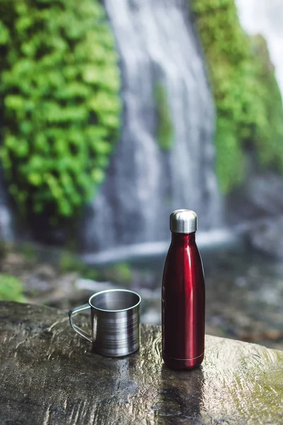 Красный термос бутылка и стальная чашка на фоне тропической ваты — стоковое фото