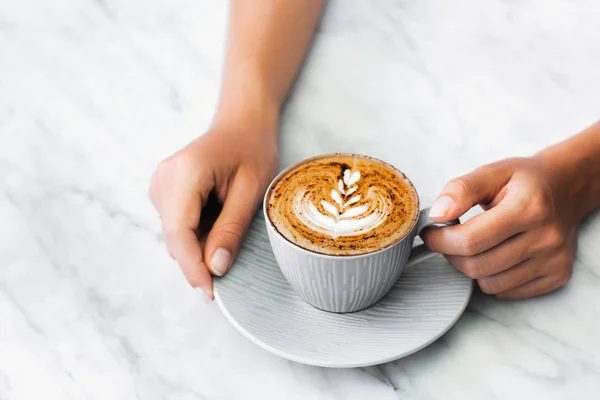 Xícara de cappuccino café fresco em mãos de mulher em mármore branco ta — Fotografia de Stock