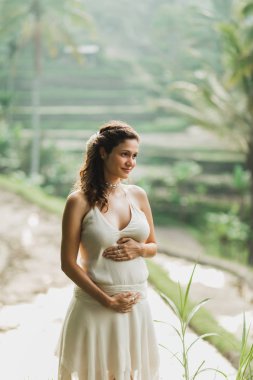 Bali pirinç tarlası manzaralı beyaz elbiseli genç hamile kadın.