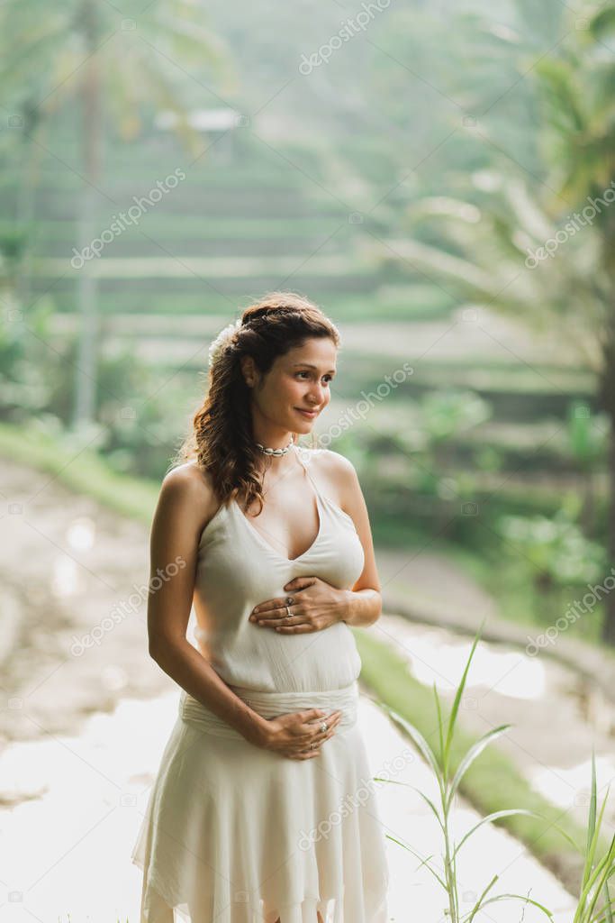 Young pregnant woman in white dress with view of Bali rice terra