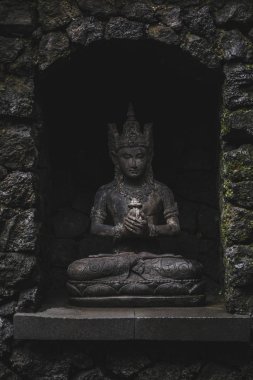 Koyu taştan arka planda Balili tanrı heykelciği. Hindu kültürü