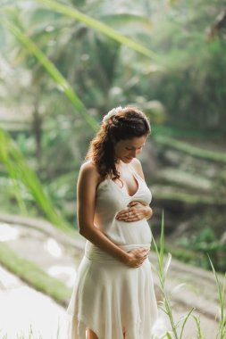 Young pregnant woman in white dress with view of Bali rice terra clipart