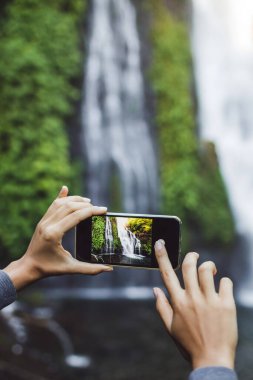 Bali 'de şelale Banyumala' nın fotoğrafını çeken kadın elleri. Seyahat kavramı.