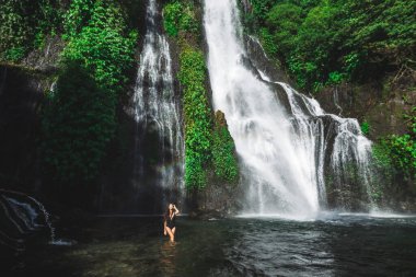 Kıvırcık saçlı, genç, zayıf esmer kadın Bali 'de tropik bir şelale olan Banyumala' nın gölünde eğleniyor. Siyah mayo giyiyordu. Endonezya 'da iyi tatiller. Seyahat konsepti.