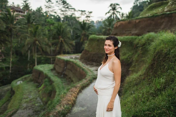 朝の日差しの中でバリの棚田を眺めながら白いドレスを着た若い妊婦 自然との調和 妊娠概念 — ストック写真