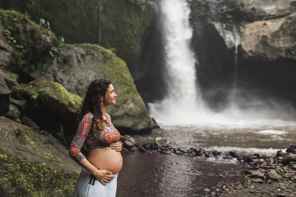 驚くべきカスケード滝の近くに若い本物の妊婦 裸の腹と白いスカート 自然との調和 インドネシアのウブドのテゲヌンガン — ストック写真