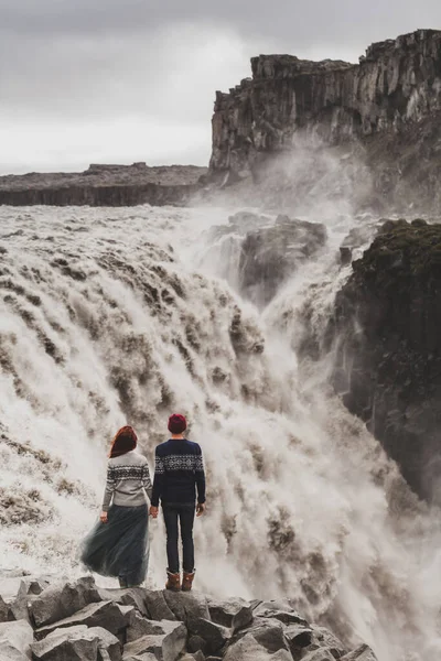 年轻夫妇相爱地看着著名的冰岛人划时代的地标式瀑布 传统羊毛衫 红头发 灰色裙子 戏剧化的北欧风景 寒冷的冰岛天气 从后面看 — 图库照片