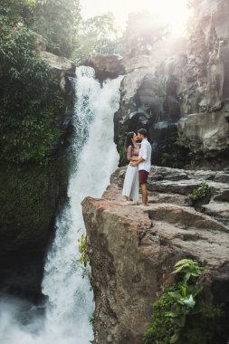 Genç çift öpüşürken Tegenungan çağlayan şelalesinin muhteşem manzarasını görüyorlar. Bali 'de mutlu bir balayı. Seyahat yaşam tarzı.