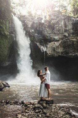 Genç çift öpüşürken Tegenungan çağlayan şelalesinin muhteşem manzarasını görüyorlar. Bali 'de mutlu bir balayı. Seyahat yaşam tarzı.