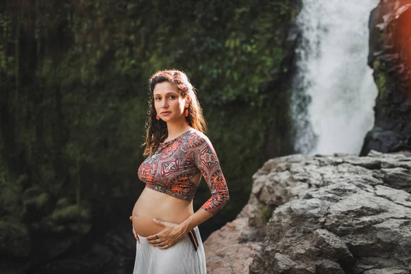 驚くべきカスケード滝の近くに若い本物の妊婦 裸の腹と白いスカート 自然との調和 インドネシアのウブドのテゲヌンガン — ストック写真