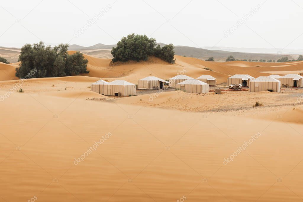 Contemporary luxury glamping camp in Morocco Sahara desert.  Sand dunes around. Many white modern eco tents.