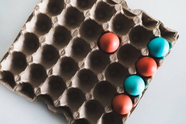 Beyaz arka planda karton kutuya boyanmış paskalya yumurtaları. Modaya uygun mavi ve kırmızı renk. Üst Manzara. Paschal konsepti.