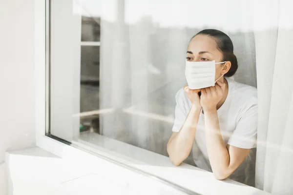 Pencereden bakan maskeli yorgun bir doktor. Önemli bir iş ve koronavirüs salgını sırasında kendini izole etmek. İlaç umudu.