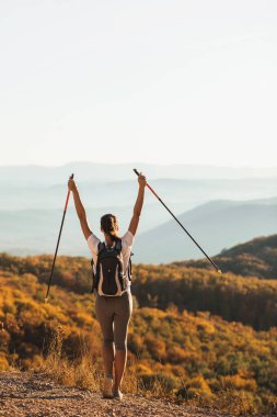 Dağın tepesine tırmanmaktan ve yürüyüş direğini tutmaktan mutluluk duyan bir kadın. Kuzeyli dışarıda yürüyor, arkadan bakıyor. Seyahat yaşam tarzı. Başarı hedef başarısı.