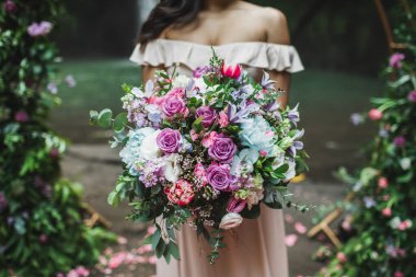 Gelin, düğün töreninde inanılmaz büyük bir çiçek buketi tutuyor. Pembe güller, şakayıklar, kırmızı laleler ve yeşiller yakın.