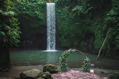 Round bronze wedding arch decorated with pink roses and greens. Unusual location for ceremony near small waterfall in jungle. Tibumana, Bali, Ubud. clipart