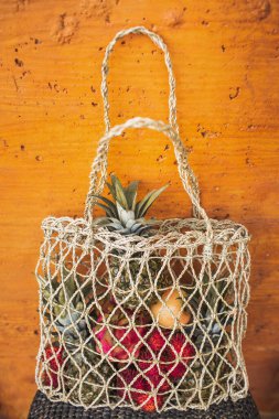 Turuncu arka planda taze organik tropikal meyveler bulunan yeniden kullanılabilir ağ torbası. Sıfır israf yaşam tarzı. Çiğ yemek ve vejetaryen diyeti.