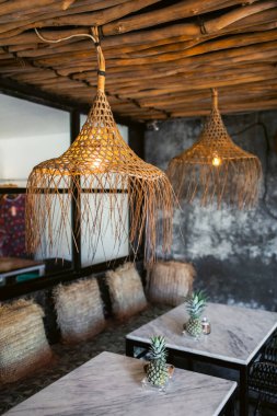 Moda tavan arası hipster kafe iç tasarımı. Beyaz mermer masalar, hasır saman lambaları ve yastıklar, bambu çatı, gri beton duvarlar..