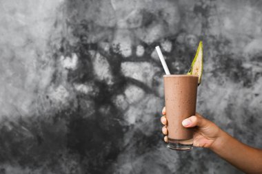 Bir bardak taze çikolatalı milkshake, arka plandaki gri beton desenli duvarda, kadınların ellerinde. Süs olarak muz parçalı kakao kokteyli. Yaz konsepti.