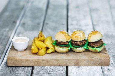 Tahta tahtada üç mini burger, patates kızartması ve mayonez. Eski püskü masa altyapısı. Sıra dışı yemek servisi. Fast food ve sağlıksız yaşam tarzı.