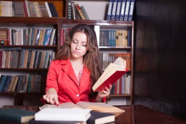 Kız kütüphanede kitap okuyor.