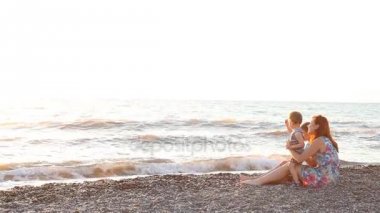 Anne ile oğlu deniz ile bir plaj gün batımında oturan iki çocuk