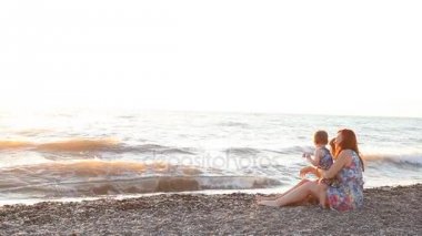 Anne ile oğlu deniz ile bir plaj gün batımında oturan iki çocuk