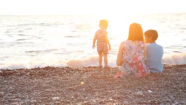 Mamma med två pojkar sitter på en strand med söner havet i solnedgången — Stockvideo
