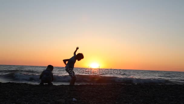Sylwetka dwóch chłopców rzucanie kamieni do morza na plaży — Wideo stockowe