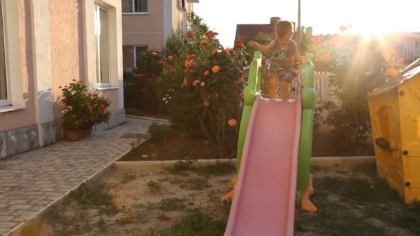 Маленький хлопчик грає на дитячому майданчику ковзає вниз з пагорба — стокове відео