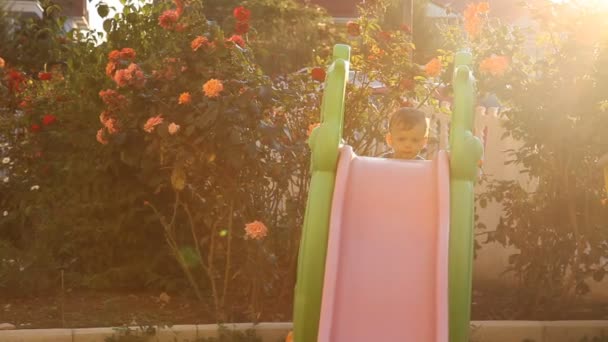 Mały chłopiec gra na placu zabaw ześlizguje się z górki — Wideo stockowe