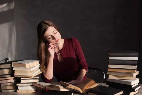 Девушка, сидящая за столом и читающая много книг — стоковое фото