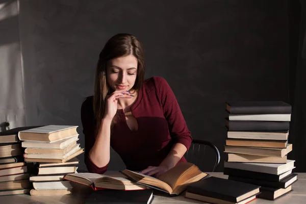 La fille assise à la table lisant beaucoup de livres — Photo