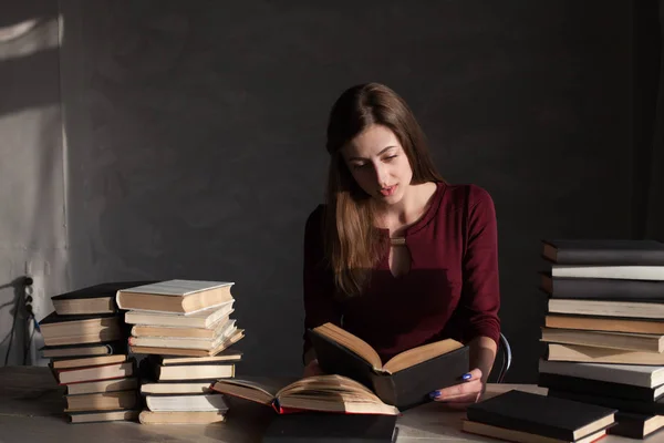 A menina sentada à mesa lendo um monte de livros — Fotografia de Stock