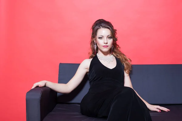 Siyah gece elbisesi kırmızı odada kanepede oturuyor ve güzel kızı — Stok fotoğraf