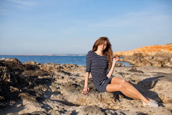 Girl sits on the rocky beach enjoys sunshine — Stock Photo, Image