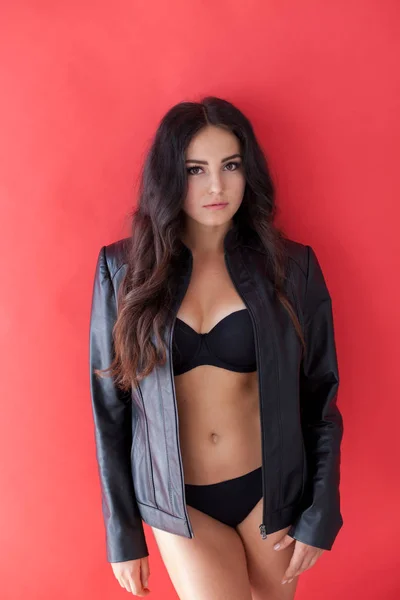 Brunette girl in leather jacket and black lingerie on a red background — Stock Photo, Image
