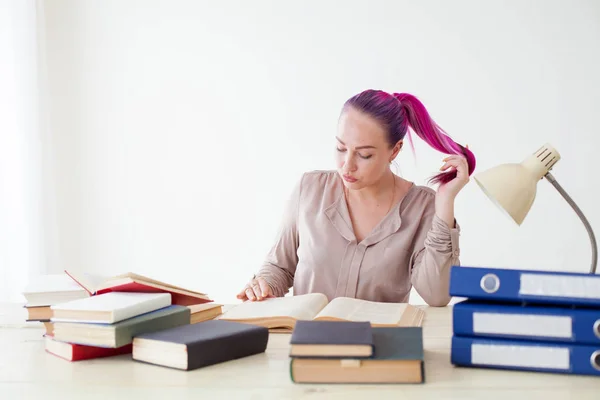 Chica con el pelo rosa sentado en una mesa leyendo un libro — Foto de Stock