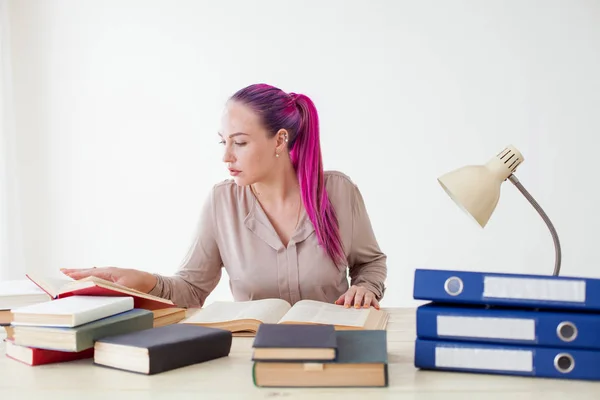 Chica con el pelo rosa sentado en una mesa leyendo un libro — Foto de Stock