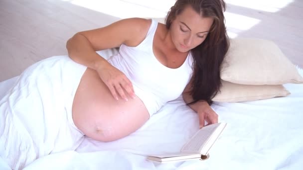 Mulher grávida encontra-se na cama lendo um livro parto — Vídeo de Stock