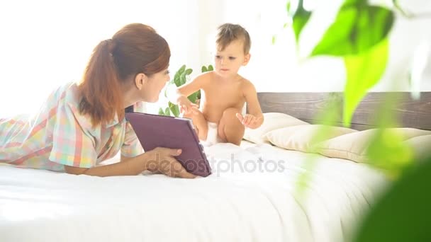 Matka a mladý syn ležet na posteli a používat Internet v tabletu — Stock video