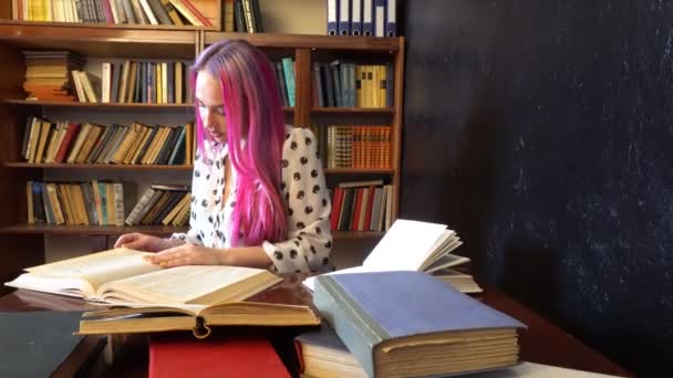 A menina com o cabelo rosa na biblioteca lendo livros — Vídeo de Stock