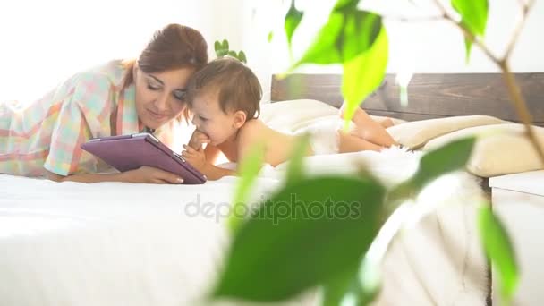 matka a mladý syn ležet na posteli a používat Internet v tabletu