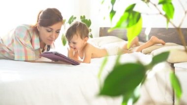 Anne ve genç oğlu yatağa uzanıp Internet Tablet kullanımı