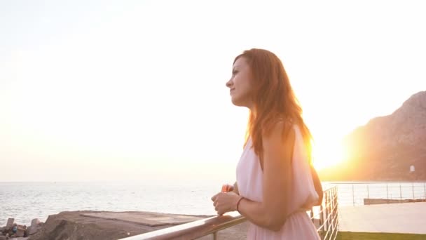 Κορίτσι στο θέρετρο στέκεται δίπλα στη θάλασσα στο ηλιοβασίλεμα — Αρχείο Βίντεο