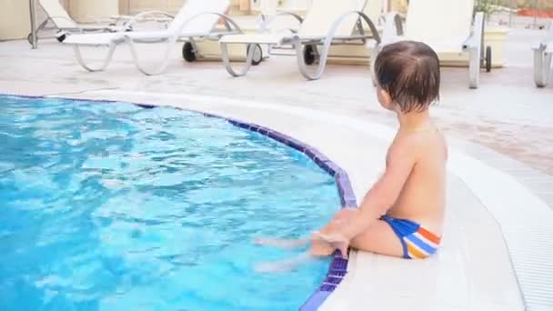 O menino está sentado junto à piscina no resort — Vídeo de Stock